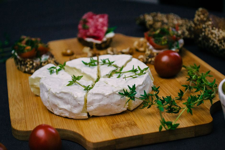 Appetizing cheese platter featuring camembert, herbs, and fresh tomatoes on a wooden board.