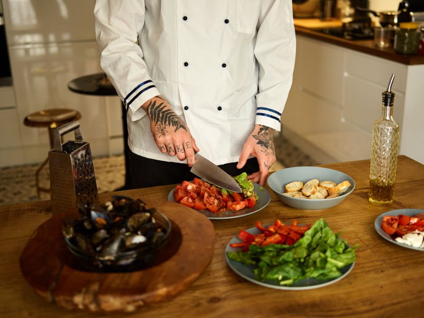 Chef prepares fresh vegetables on wooden table in modern kitchen setting.